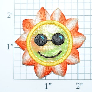 May include: A yellow embroidered sun with a smiling face and sunglasses. The sun has orange and white petals.