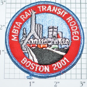 May include: A red, white, and blue embroidered patch with the text "MBTA Rail Transit Rodeo Boston 2001". The patch features a stylized image of a train on a bridge.