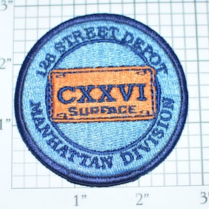 May include: Blue and orange embroidered patch with the text "128 STREET DEPOT MANHATTAN DIVISION" and "CXXVI SURFACE" inside a license plate shape.