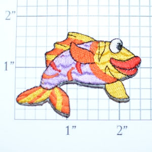 May include: A colorful embroidered iron-on patch of a cartoon fish with orange, yellow, and purple stripes. The fish has a big smile and a large eye.