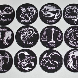 May include: Twelve black and white embroidered patches featuring the astrological signs of the zodiac. Each patch has a white design on a black background. The signs are: Aquarius, Aries, Cancer, Gemini, Leo, Libra, Pisces, Sagittarius, Scorpio, Taurus, Virgo, and Capricorn.