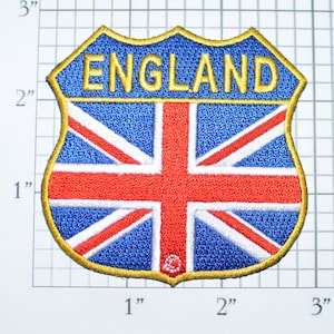 May include: A 2-inch embroidered patch with a shield shape. The shield is blue with a red, white, and blue Union Jack flag design. The word "ENGLAND" is embroidered in yellow at the top of the shield.