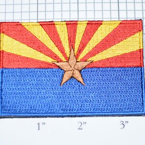 May include: An embroidered patch of the Arizona state flag. The flag is red, yellow, and blue with a star in the center. The patch is approximately 2 inches by 3 inches.