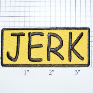 May include: A yellow rectangular patch with a black outline and the word "JERK" embroidered in black.
