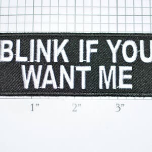 May include: Black embroidered patch with white text that reads "Blink if you want me". The patch is approximately 1 inch by 3 inches.