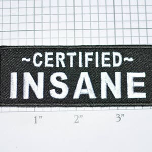 May include: Black rectangular patch with white embroidered text that reads "~CERTIFIED~ INSANE". The patch is approximately 4 inches long and 1 inch tall. The background is a grid.
