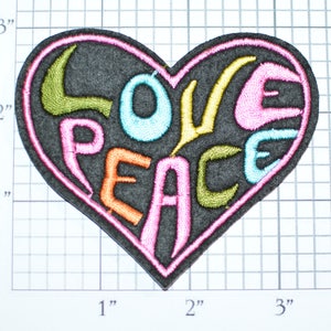 May include: A pink heart-shaped patch with the words "LOVE PEACE" embroidered in colorful thread. The letters are outlined in black and the heart is outlined in pink.