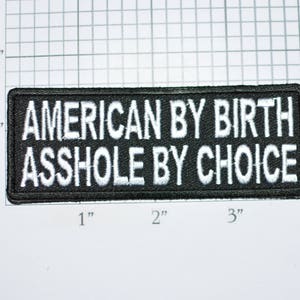 May include: Black and white embroidered patch with the text "AMERICAN BY BIRTH ASSHOLE BY CHOICE".