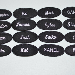 May include: A set of 16 black oval-shaped patches with white embroidered text. The names on the patches are Alexander, Ed, Matt, SANJO, Brandon, James, Rylee, Stephon, Bryce, Josh, Saiko, Tim, Devin, Kal, SANEL, and Will.