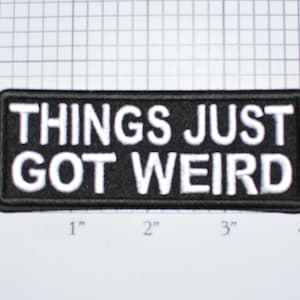 May include: Black and white embroidered patch with the text "Things Just Got Weird" on a black background. The patch is approximately 3 inches wide and 1 inch tall.