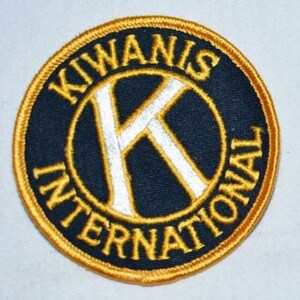 May include: A gold and black embroidered patch with the text "KIWANIS INTERNATIONAL" and a white "K" in a circle.