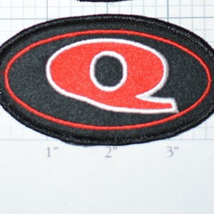 May include: Red embroidered letter Q in a white outline, on a black oval patch with a red border. The patch is approximately 2 inches wide and 1 inch tall.