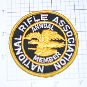 May include: A gold and black embroidered patch with the text "National Rifle Association Annual Member" and a stylized eagle design.