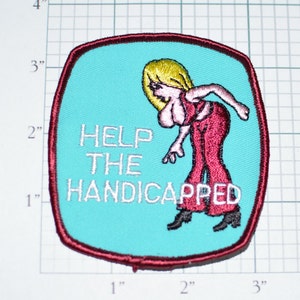 May include: A turquoise blue embroidered patch with a red border. The patch features a cartoon woman in red pants and a red top with the text "HELP THE HANDICAPPED" in white.