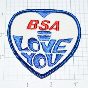 May include: A white heart-shaped patch with blue embroidered lettering that says "BSA LOVE YOU" and a red embroidered "BSA" above the lettering.