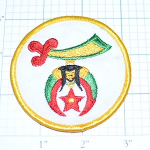 May include: A white embroidered patch with a gold border, featuring a red, green, and yellow crescent moon with a red star in the center. A red and yellow figure with a green sash hangs from the crescent moon.
