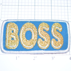May include: A blue and white embroidered iron-on patch with the word "BOSS" in gold glitter lettering.