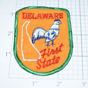 May include: A vintage embroidered patch featuring a white rooster with blue accents, a white outline of the state of Delaware, and the text "DELAWARE First State". The patch is orange with a green border.