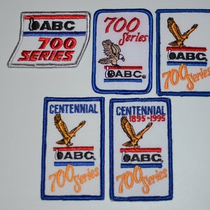 May include: Five embroidered patches featuring a golden eagle, the text "ABC 700 Series", and the text "Centennial 1895-1995".