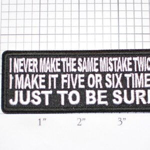 May include: A rectangular black patch with white embroidered text. The text reads: "I NEVER MAKE THE SAME MISTAKE TWICE I MAKE IT FIVE OR SIX TIMES JUST TO BE SURE."