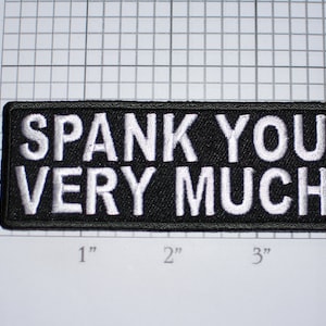 May include: Black embroidered patch with white text that reads "SPANK YOU VERY MUCH".
