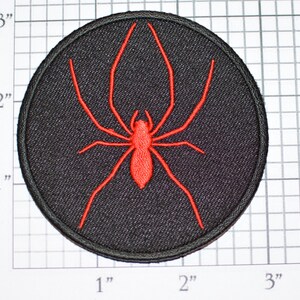 May include: Red embroidered spider patch on a black circular background. The patch is approximately 2 inches in diameter.