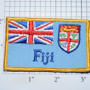 May include: A blue and gold embroidered patch with the Fijian flag and the word "Fiji" on a light blue background.
