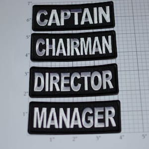 May include: Four black fabric patches with white embroidered text. The patches read "CAPTAIN", "CHAIRMAN", "DIRECTOR", and "MANAGER".