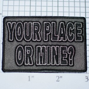 May include: Gray embroidered patch with black outline. The patch reads "YOUR PLACE OR MINE?"
