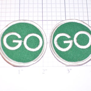 May include: Two green and white embroidered patches with the word "GO" in white on a green background. Each patch is approximately 1.5 inches in diameter.