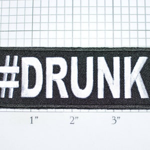 May include: A rectangular black patch with white embroidered text that reads "#DRUNK". The patch is approximately 4 inches long and 1 inch tall.
