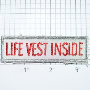 May include: White embroidered patch with silver thread outlining the edges. The patch reads "LIFE VEST INSIDE" in red thread.