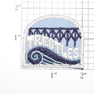 May include: A blue and white embroidered patch with the word "Trestles" and a stylized image of a bridge. The patch is approximately 1.5 inches wide and 2 inches tall.