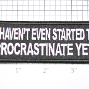 May include: Black rectangular patch with white text that reads "I HAVEN'T EVEN STARTED TO PROCRASTINATE YET!". The patch measures approximately 4 inches long and 1 inch tall.