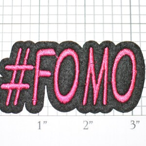 May include: A black felt patch with pink embroidered text that reads "#FOMO".