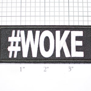 May include: Black embroidered patch with white stitching that reads "#WOKE" in all caps. The patch is approximately 3 inches wide and 1 inch tall.