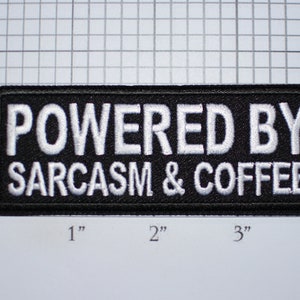 May include: Black embroidered patch with white text that reads "POWERED BY SARCASM & COFFEE". The patch is approximately 3 inches wide and 1 inch tall.