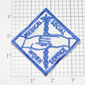 Puede incluir: Un parche blanco en forma de diamante con un borde azul. El parche presenta un símbolo médico azul con dos manos entrelazadas a su alrededor. El texto "MEDICAL WORK SOCIAL SERVICE" está escrito alrededor del símbolo.
