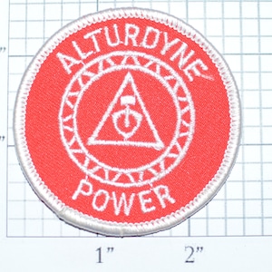 May include: A red and white embroidered patch with the text "ALTURDYNE POWER" in a circle around a white triangle with a stylized power button inside. The patch is approximately 2 inches in diameter.