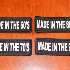 May include: Four black fabric patches with white text. The patches read "Made in the 60's", "Made in the 70's", "Made in the 80's", and "Made in the 90's".