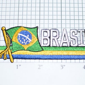 May include: Embroidered patch featuring the Brazilian flag with the word "BRASIL" in white lettering. The flag is green, yellow, and blue with a blue circle in the center. The patch is approximately 4 inches wide.