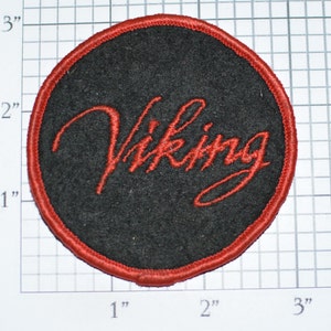 May include: A red and black round embroidered patch with the word "Viking" in red cursive lettering.