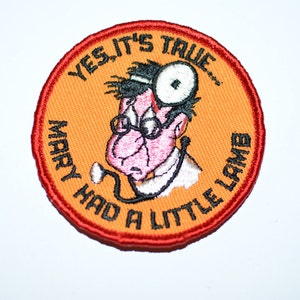 May include: A round orange and red embroidered patch with a cartoon doctor wearing glasses and a stethoscope. The text on the patch reads "Yes, it's true... Mary had a little lamb."