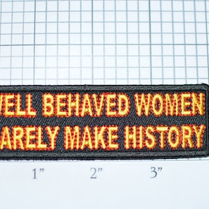 May include: Black embroidered patch with yellow and red stitching. The patch reads "WELL BEHAVED WOMEN RARELY MAKE HISTORY".