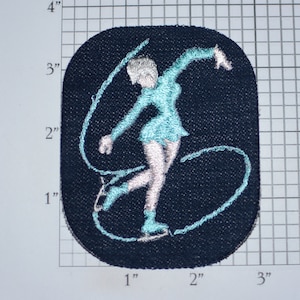 May include: Embroidered patch featuring a figure skater in a teal dress and silver hair, executing a graceful pose with a ribbon. The patch is approximately 3 inches tall and 2 inches wide, set against a dark blue background.