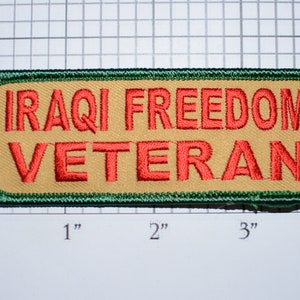 May include: A tan fabric patch with green edging. The text "IRAQI FREEDOM VETERAN" is embroidered in red.