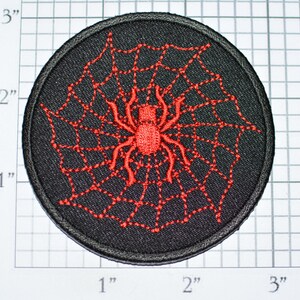 May include: Round black patch with a red spider and web design. The spider and web are embroidered on the patch. The patch is approximately 3 inches in diameter.
