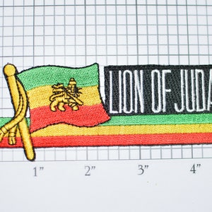 May include: An embroidered patch with a green, yellow, and red flag with a lion in the center. The flag is next to a black rectangle with the text "LION OF JUDAH" in white.