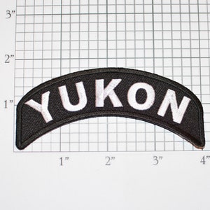 May include: Black and white embroidered patch with the word "YUKON" in white lettering on a black background. The patch is curved and measures approximately 3 inches wide.