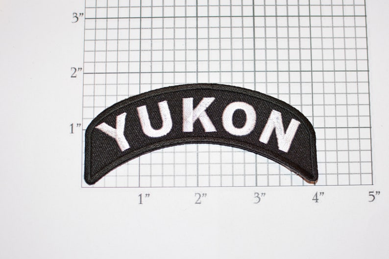 May include: Black and white embroidered patch with the word "YUKON" in white lettering on a black background. The patch is curved and measures approximately 3 inches wide.